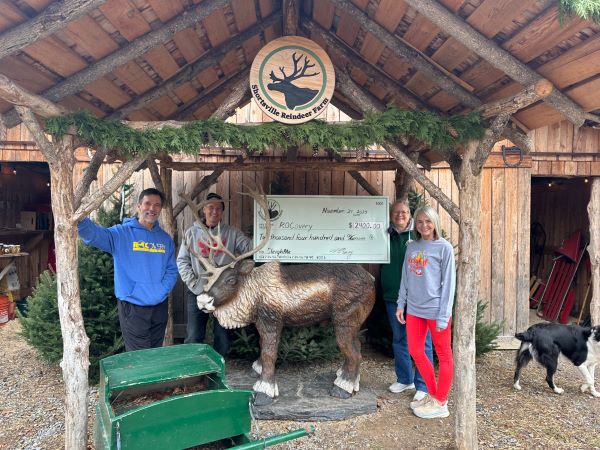 People with a giant check presentation in front of a reindeer statue.