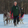 A man leading a reindeer pulling a sleigh.
